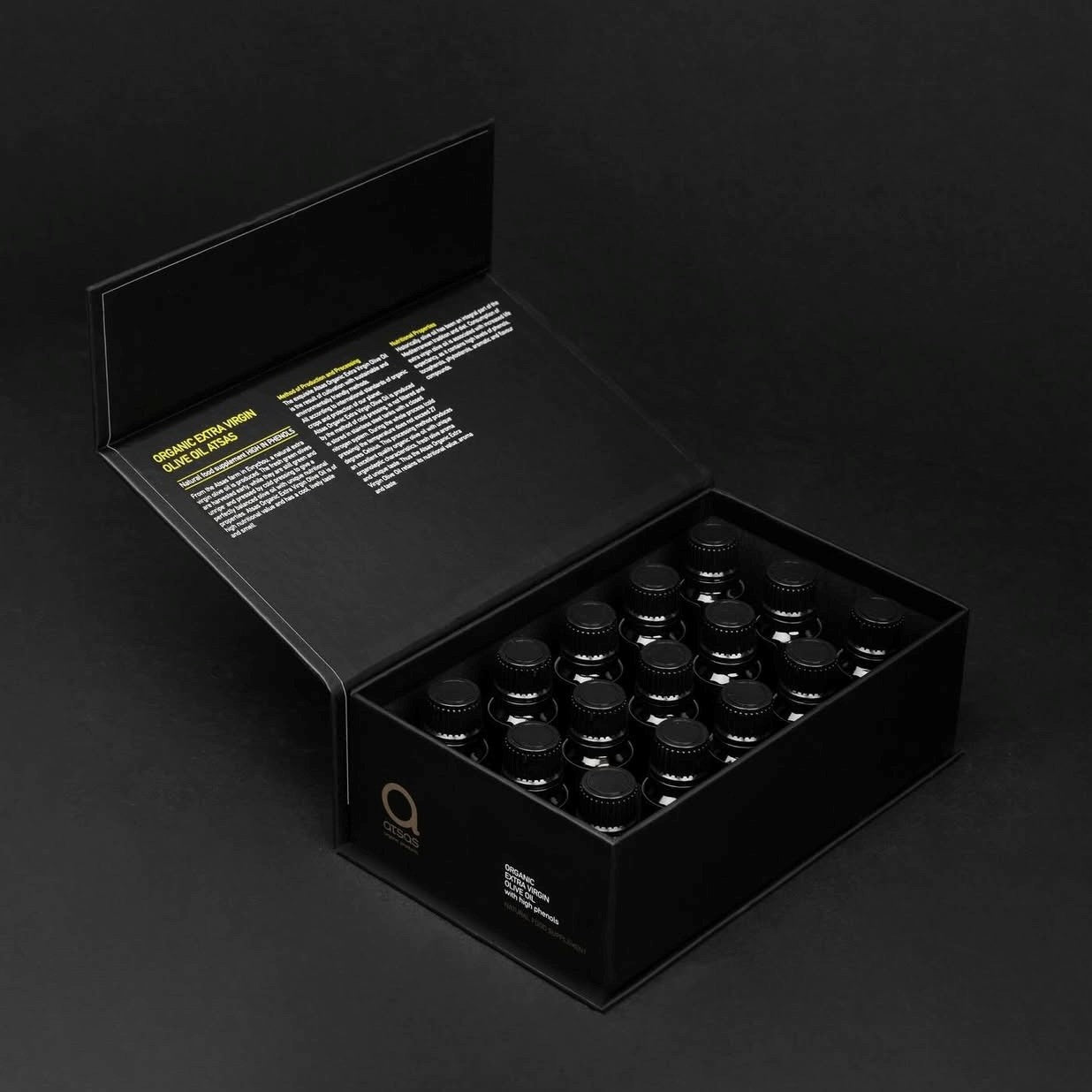 Black box containing multiple small dark bottles of olive oil on a black background